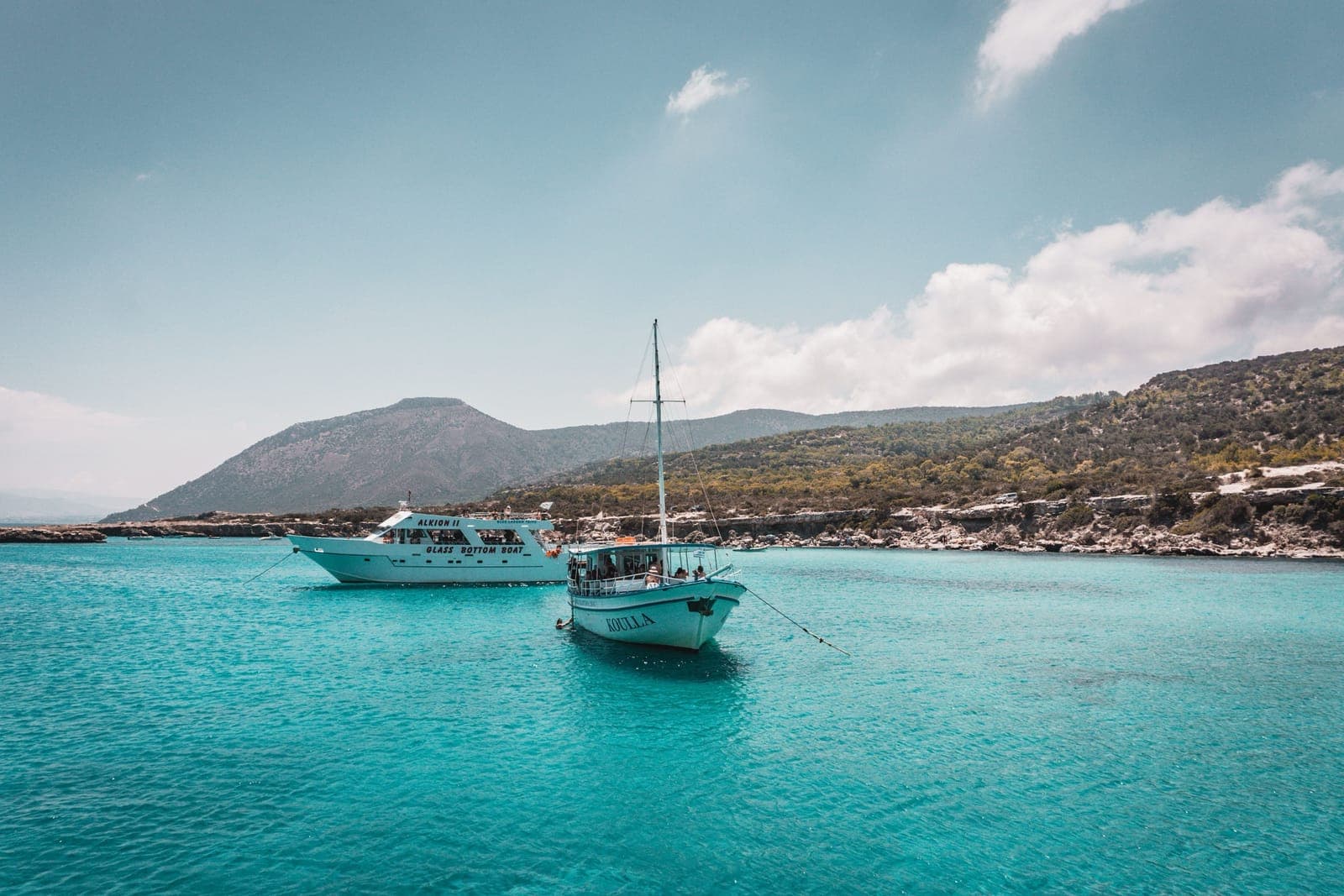 Tour boats anchored in the turquoise water of the Blue Lagoon, with the scrub-covered, undeveloped hills of the Akamas peninsula behind