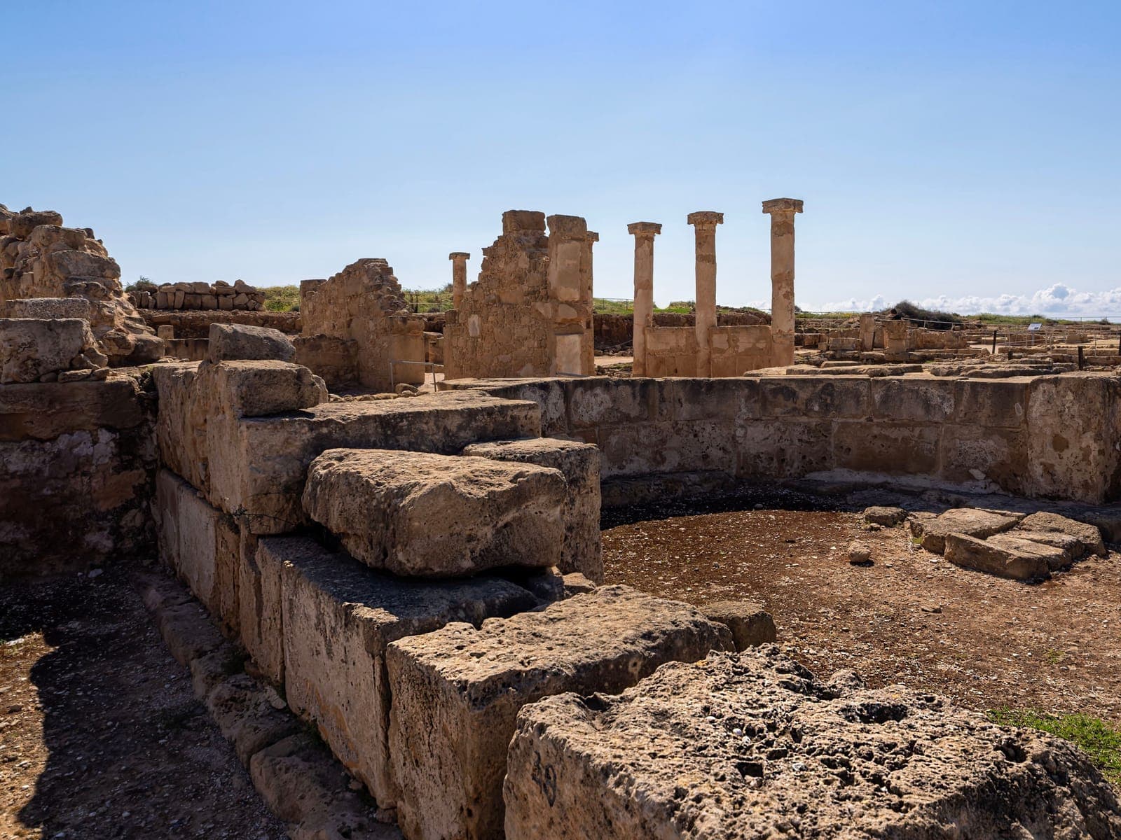 Standing Roman columns and limestone walls among the excavated ruins of Nea Paphos in the Kato Paphos Archaeological Park, under a clear sky