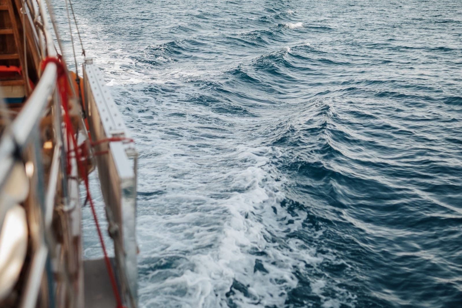 View over the side of a wooden tour boat at sea, its wake churning white against deep blue water