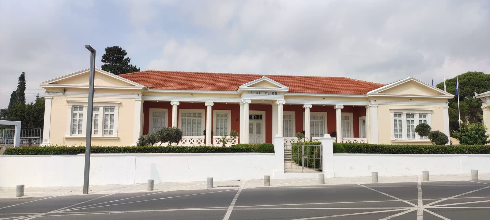 The neoclassical Dimitreion building in Paphos, with Ionic columns, a red-tiled roof and a white wall along the street