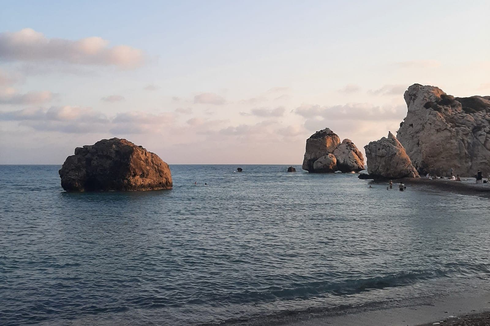 Petra tou Romiou at sunset: the sea stacks of Aphrodite's Rock and the white limestone headland seen from the pebble beach, with a few swimmers