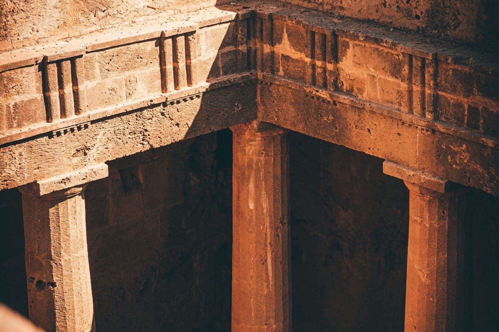 Looking down into a rock-cut peristyle tomb at the Tombs of the Kings, with Doric columns and a carved triglyph frieze around the sunken courtyard